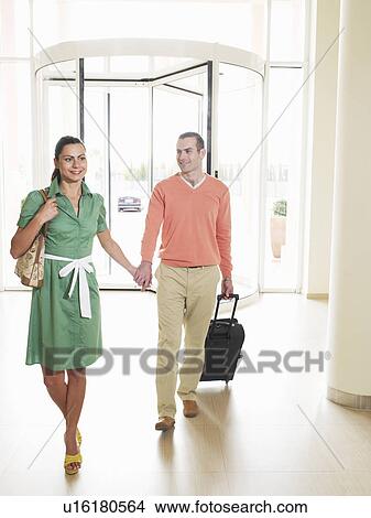 Picture - Couple arriving at hotel holding hands, smiling. Fotosearch