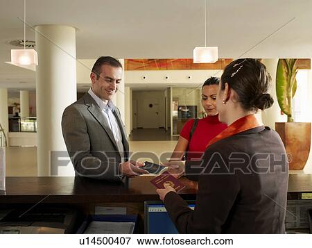 Stock Photo - Couple handing passports to female hotel receptionist. Fotosearch