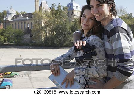 Couple holding binoculars and a map outdoors smiling. View Large Photo Image Stock Photo - Couple holding binoculars and a map outdoors smiling.. Fotosearch