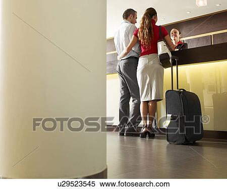 Stock Photography - Couple standing at hotel reception, rear view. Fotosearch