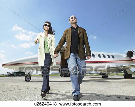 Stock Photo - Happy couple walking away from private jet.. Fotosearch