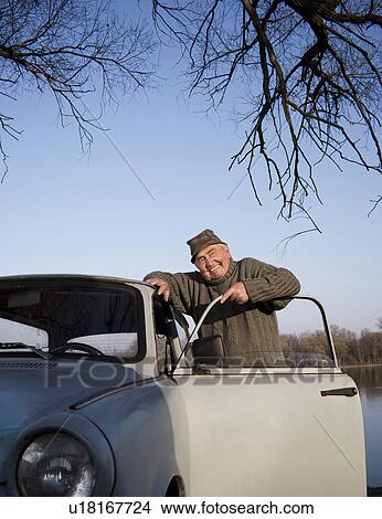 Senior man standing by car on riverside, smiling, portrait View Large Photo Image Picture - Senior man standing by car on riverside, smiling, portrait. Fotosearch