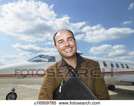 Stock Photography - Smiling man standing next to private jet.. Fotosearch