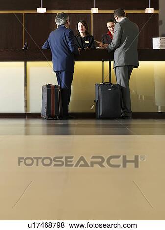 Two businessmen standing at hotel reception View Large Photo Image Stock Photo - Two businessmen standing at hotel reception. Fotosearch