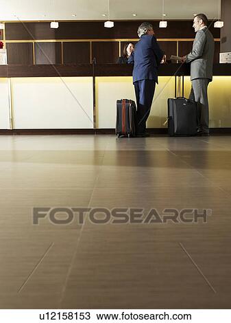 Two businessmen standing talking at hotel reception View Large Photo Image Stock Image - Two businessmen standing talking at hotel reception. Fotosearch