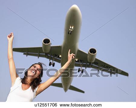 Woman smiling with arms outstretched standing below a plane flying overhead. View Large Photo Image Stock Photograph - Woman smiling with arms outstretched standing below a plane flying overhead.. Fotosearch