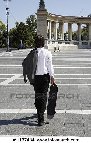 Picture - Business walking holding skateboard.. Fotosearch