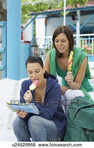 Two smiling women sitting on steps while looking at map and eating Popsicles. View Large Photo Image Stock Photo - Two smiling women sitting on steps while looking at map and eating Popsicles.. Fotosearch