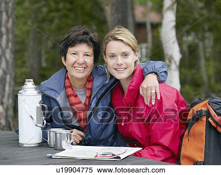 Two women sitting at a table with a thermos and map smiling. View Large Photo Image Stock Photography - Two women sitting at a table with a thermos and map smiling.. Fotosearch