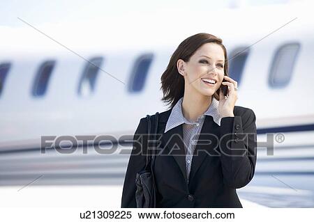 Stock Photography - A business woman talking on a mobile phone next to a plane. Fotosearch