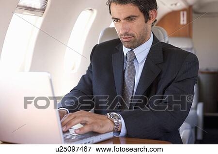 Stock Photo - A businessman using a laptop in a plane. Fotosearch