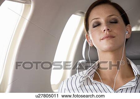 Stock Image - A businesswoman listening to music on a flight. Fotosearch
