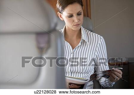 Stock Photo - A passenger reading a magazine on a flight. Fotosearch
