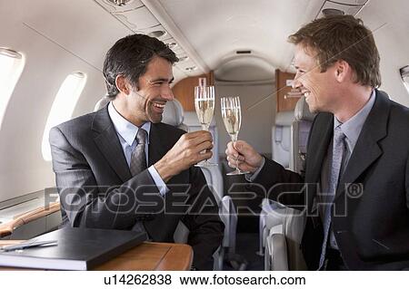 Two businessmen drinking champagne on a flight View Large Photo Image Stock Photo - Two businessmen drinking champagne on a flight. Fotosearch