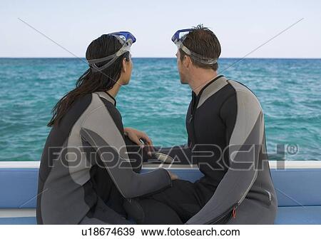Stock Photo - A couple sitting on a boat preparing to go scuba diving. Fotosearch