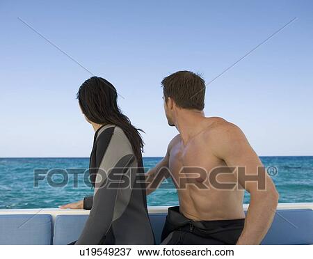 Stock Photo - A couple sitting on a boat preparing to go scuba diving. Fotosearch