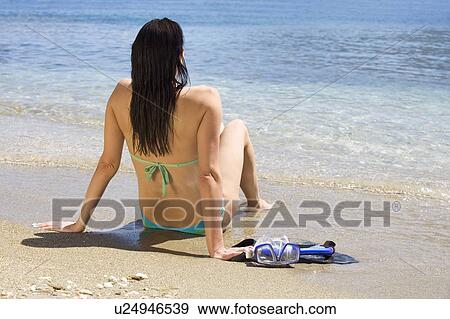A woman sitting on a beach in a bikini View Large Photo Image Stock Photo - A woman sitting on a beach in a bikini. Fotosearch