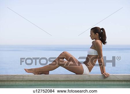 Picture - A young woman sitting on the edge of a pool. Fotosearch