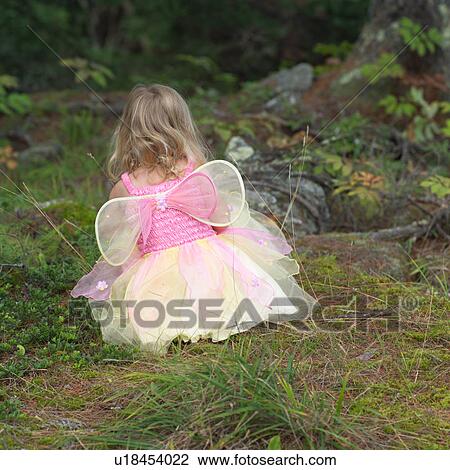 Stock Image - Rear view of a young girl in a fairy costume squatting in the grass. Fotosearch