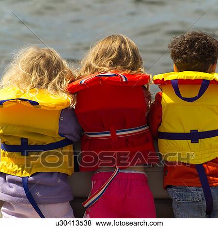 Rear view of three young children standing side by side wearing life jackets View Large Photo Image Stock Photo - Rear view of three young children standing side by side wearing life jackets. Fotosearch