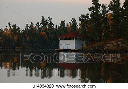 Stock Image - White Boathouse Reflected in Lake. Fotosearch