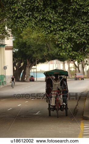 Stock Image - A man riding a Pedicab on the road, Havana, Cuba. Fotosearch