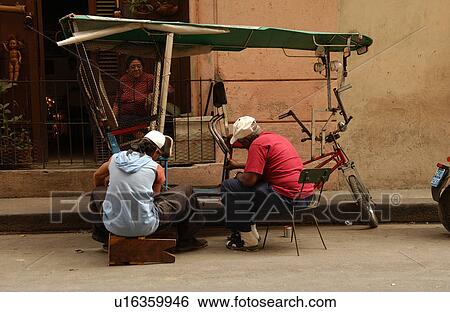 Stock Photograph - Rear view of two men repairing a Pedicab, Havana, Cuba. Fotosearch