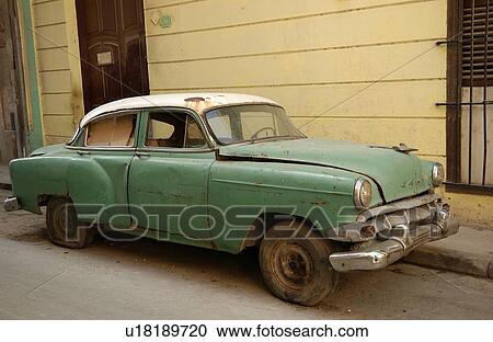 Stock Image - A building structure with an antique car parked in front, Havana, Cuba. Fotosearch