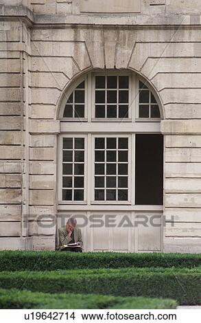Picture - Man sitting reading outside a building in Paris, France. Fotosearch