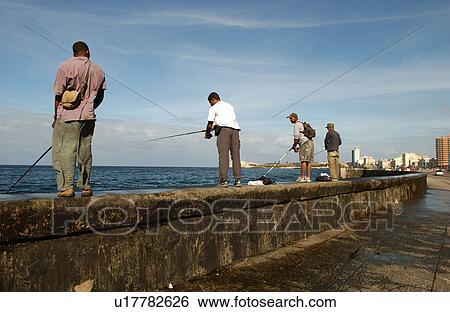 Stock Photograph - Rear view of people standing on a wall with fishing rods. Fotosearch
