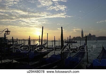 Silhouettes of gondolas docked during a sunset at a canal in Venice, Italy View Large Photo Image Stock Photo - Silhouettes of gondolas docked during a sunset at a canal in Venice, Italy. Fotosearch