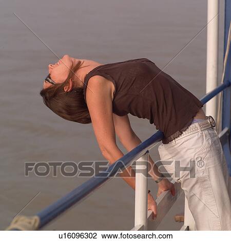 Stock Image - Brunette woman bending backwards over a railing. Fotosearch