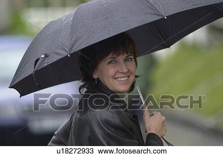 Stock Image - Portrait of young woman smiling holding an umbrella in Prague. Fotosearch