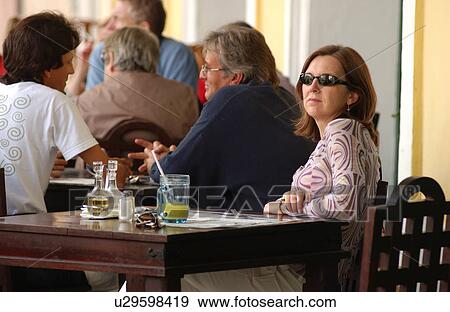 Stock Photo - View of a woman sitting at a table in an outdoor cafe. Fotosearch