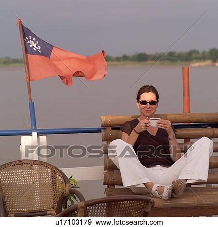 Stock Photo - Woman sitting on a boat holding a beverage. Fotosearch