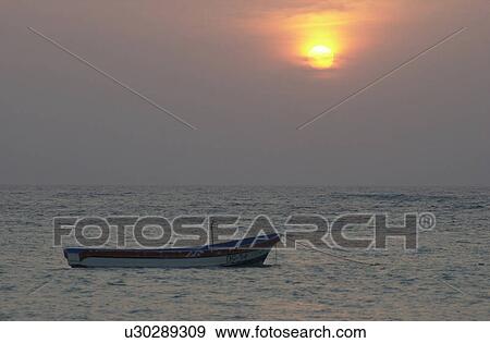 Stock Photo - A boat floating on the sea in Mexico during sunset. Fotosearch