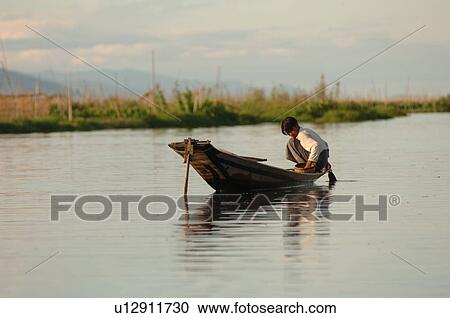 Stock Image - Boy crouching in boat. Fotosearch