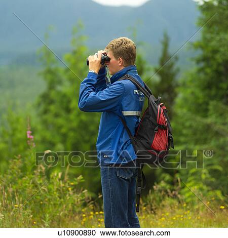 Stock Image - Hiker looking through binoculars, Pacific Rim National Park, Vancouver Island, Canada. Fotosearch