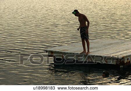 Stock Image - A young man looking into the water standing on a raft. Fotosearch