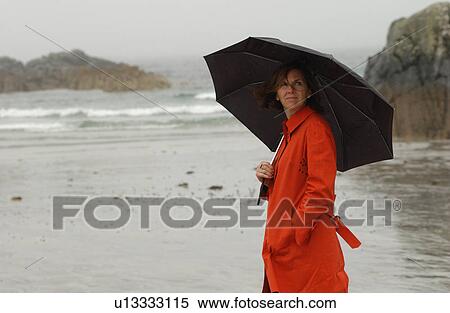 Portrait of a woman holding an umbrella and standing on the beach View Large Photo Image Stock Photography - Portrait of a woman holding an umbrella and standing on the beach. Fotosearch