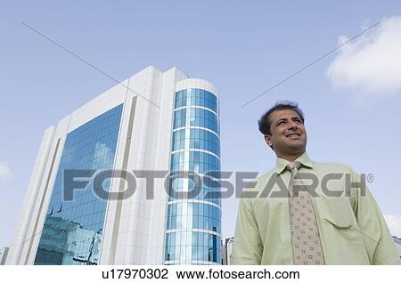 Stock Image - Low angle view of a businessman standing in front of a building. Fotosearch