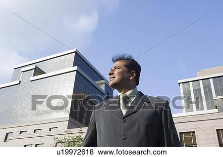 Stock Photo - Low angle view of a businessman standing in front of a building. Fotosearch