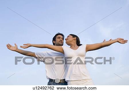 Low angle view of a young couple standing together with their arms outstretched and smiling View Large Photo Image Stock Image - Low angle view of a young couple standing together with their arms outstretched and smiling. Fotosearch