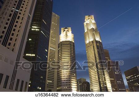 Stock Image - Low angle view of skyscrapers lit up at dusk, Singapore. Fotosearch