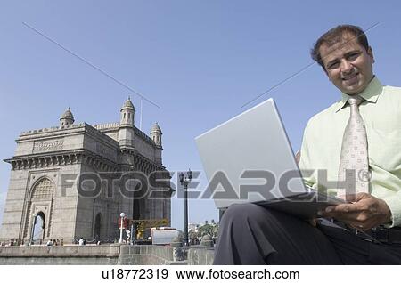 Portrait of a businessman using a laptop and smiling, Gateway of India, Mumbai, Maharashtra, India View Large Photo Image Stock Photo - Portrait of a businessman using a laptop and smiling, Gateway of India, Mumbai, Maharashtra, India. Fotosearch