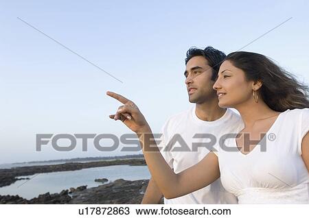 Side profile of a young woman pointing forwards with a young man standing beside her, Madh Island, Mumbai, Maharashtra, India View Large Photo Image Stock Image - Side profile of a young woman pointing forwards with a young man standing beside her, Madh Island, Mumbai, Maharashtra, India. Fotosearch
