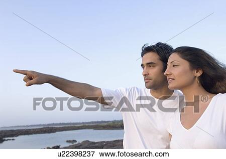 Young man pointing forward with a young woman standing beside him, Madh Island, Mumbai, Maharashtra, India View Large Photo Image Stock Photo - Young man pointing forward with a young woman standing beside him, Madh Island, Mumbai, Maharashtra, India. Fotosearch