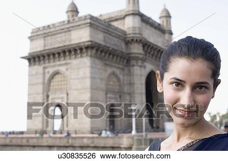 Stock Photograph - Portrait of a young woman smiling with a monument in the background, India . Fotosearch