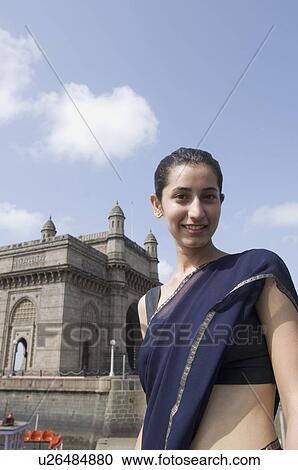 Stock Image - Portrait of a young woman standing with a monument in the background, Gateway Of India, Mumbai, Maharashtra, India. Fotosearch