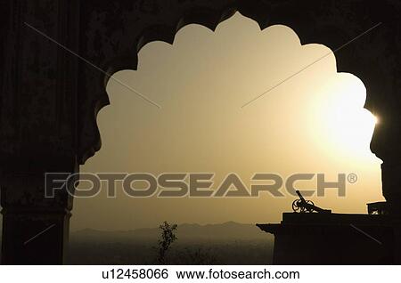 Stock Photograph - Silhouette of a cannon viewed through an arch at sunset, Neemrana Fort, Neemrana, Alwar, Rajasthan, India. Fotosearch